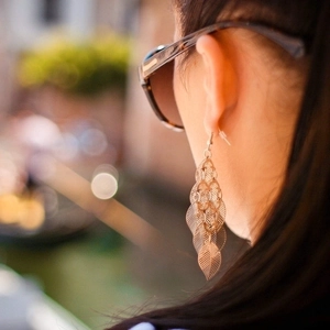 Long tassel leaf earrings in gold metallic finish worn by model in soft outdoor light