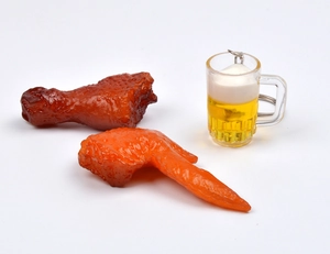 Dettaglio di portachiavi con boccale di birra e ala di pollo arrosto su sfondo bianco