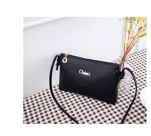 Detail of black pebbled crossbody envelope bag featuring golden leaf zipper and logo