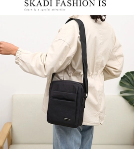 Detail view of a black oxford messenger bag with adjustable shoulder strap and metal logo