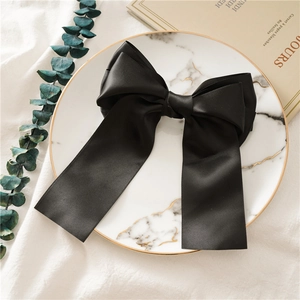 Detailed view of a black satin bow hair clip on a marble tray with eucalyptus leaves