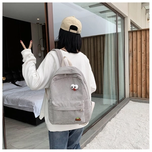 Light gray corduroy backpack with cute cartoon face detail shown on model back