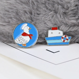 Close-up of enamel duck buoy and boat brooches set on white card and plush background