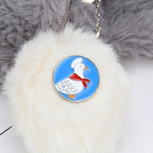 Detail of plush white keychain with blue duck badge and silver metal clasp finish