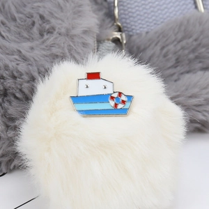 Detailed macro view of a ship-shaped enamel brooch pinned on a soft white plush pom-pom
