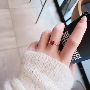 Close-up of a delicate rose gold ring with a red heart-shaped zircon on a model's finger