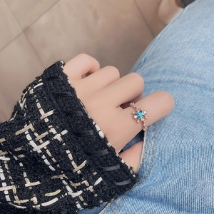 Close-up of rose gold flower ring featuring a square blue stone and crystal micro-paving