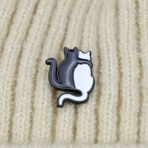 Detail of cute black and white hugging cats enamel pin on cream knit background