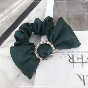 Close-up of a dark green satin scrunchie featuring a central sparkling rhinestone buckle