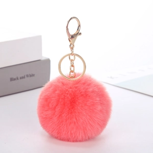 Close-up of a soft pink faux rabbit fur pom pom keychain with a polished gold clasp