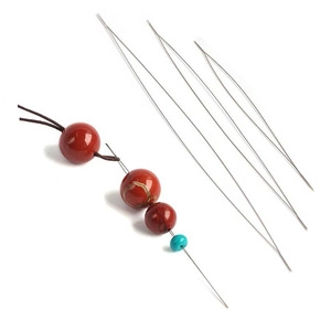 Detailed view of beading needles stringing brown and turquoise beads on a white surface