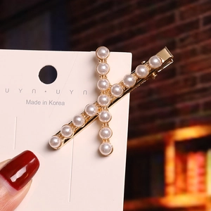 Detailed close-up of a golden X-shaped hair clip with pearls held by a manicured hand