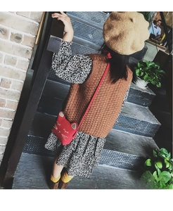 Detail of red cat-shaped crossbody bag styled with knit vest and floral girl's dress