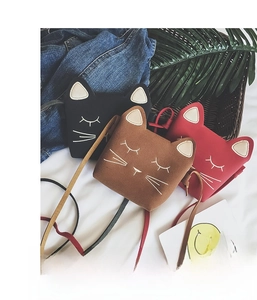 Detail of cute cat shaped mini crossbody bags in black, brown and red on soft white fabric