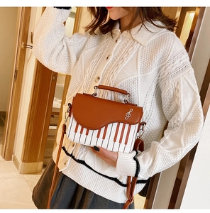 Detail of piano keyboard pattern handbag with brown leather flap and treble clef metal charm