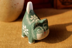 Detail of green hand-painted wooden cat ornament with white floral patterns on burlap