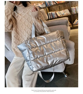 Silver quilted puffer tote bag shown in a cozy lifestyle setting with books and sweater