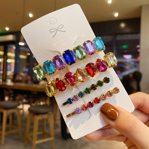Close-up of four gold hairpins with colorful rhinestones on a white display card