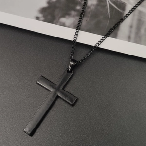 Close-up of a black metal minimalist cross pendant necklace on textured surface
