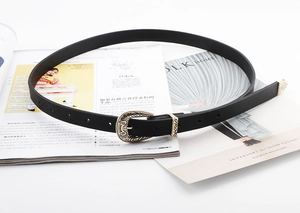 Detailed close-up of a slim black leather belt with ornate golden vintage floral buckle