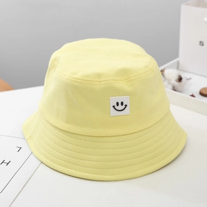 Close-up of a pale yellow cotton bucket hat featuring a white square smiley face patch