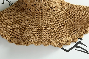 Dettaglio del cappello in paglia lavorato a mano con bordo a onde e trama traforata