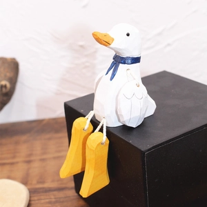 Détail d'un canard en bois avec bec jaune et écharpe bleue sur socle noir