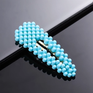 Close-up of an oval hair clip with dense blue pearlescent beads on a black surface