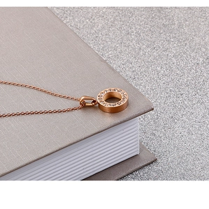 Macro shot of rose gold necklace with crystal-encrusted circular pendant on a grey book