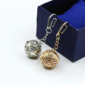 Intricate hollow sphere metal pendant keychain in silver and gold on jewelry box