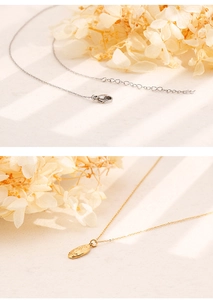 Close-up of gold oval relief pendant and lobster clasp detail on stainless steel necklace
