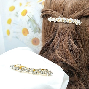 Détail de la barrette à fleurs en strass et perles sur cheveux bruns et tissu blanc