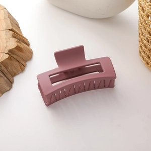 Macro detail of large matte mauve pink rectangular hollow hair claw clip on wooden block