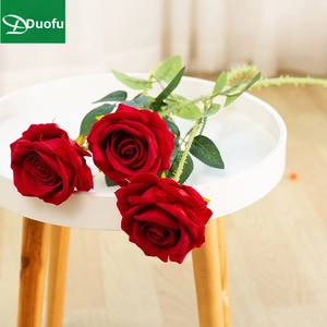 Detailed view of three artificial red roses with velvet texture on a white wooden stool