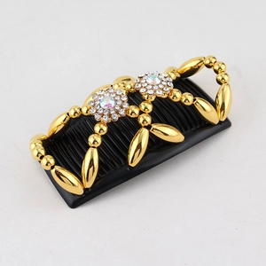 Close-up of golden magic hair comb with rhinestone flowers and black beaded double-row teeth