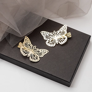 Détail de deux pinces à cheveux papillon dorées ajourées sur une boîte de présentation noire
