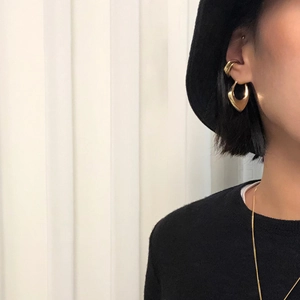 Close-up of matte gold geometric heart earring and thick ear cuff worn on model