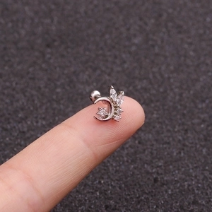 Silver crescent moon and star piercing stud with clear zircons shown on a fingertip