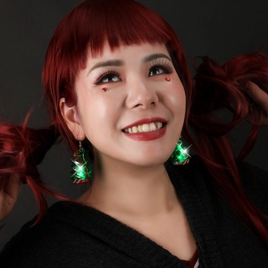 Close-up of glowing green LED Christmas tree earrings worn by a model in a dark setting