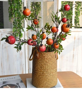 Detail of red faux pomegranates with green leaves in a woven straw basket