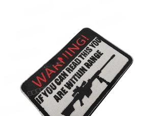Macro shot of embroidered WARNING tactical patch with rifle silhouette and red lettering