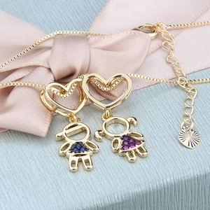 Detail view of gold necklaces with boy and girl heart pendants on a blue gift box