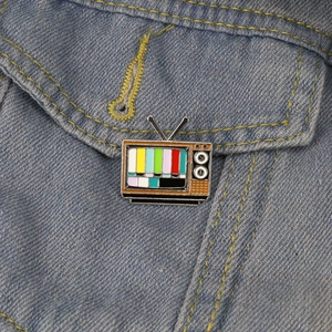 Retro TV enamel pin with colorful signal bars on a classic blue denim jacket pocket