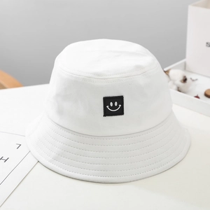Detailed view of kids' white canvas bucket hat with a minimalist black smiley face patch