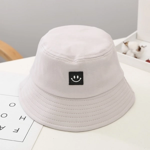Close-up of beige cotton bucket hat with black square smiley patch and stitched brim