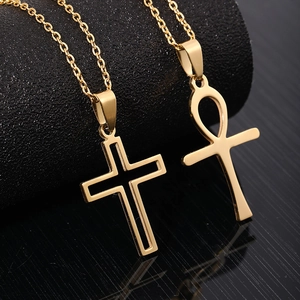Polished gold stainless steel cross and Ankh pendant necklaces on a black mirrored surface