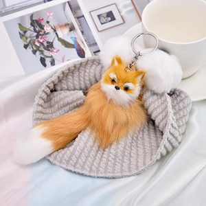 Fluffy plush fox keychain with orange fur and white pom-poms on a grey knit hat
