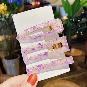 Close-up of three purple resin hair clips with gold metal bases in various shapes