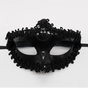 Detail of a black masquerade mask with top faceted gem, lace trim and sparkling sequins