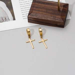 Close-up of golden stainless steel cross pendant earrings with polished finish on wooden stand